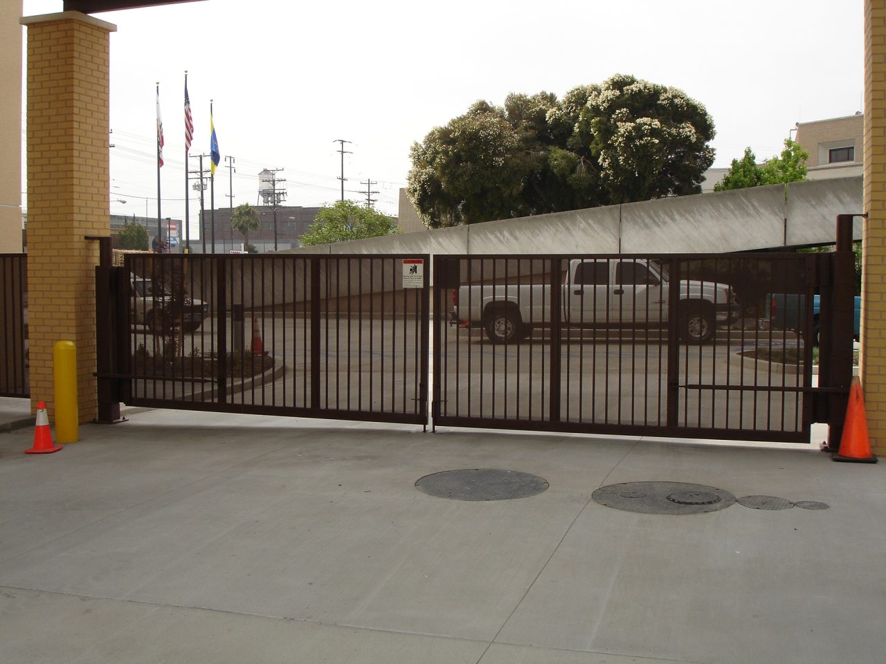 Dark brown steel bar sliding vehicle gate at a commercial facility entrance with brick columns and traffic cones