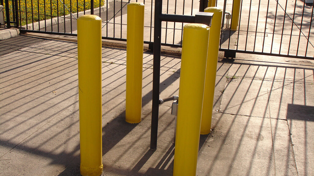 Row of fixed yellow security bollards beside a gated entrance
